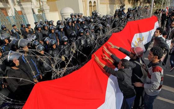 Protesters place a large banner screen in front of razor wire and riot cops, Cairo, Jan 25, 2013.